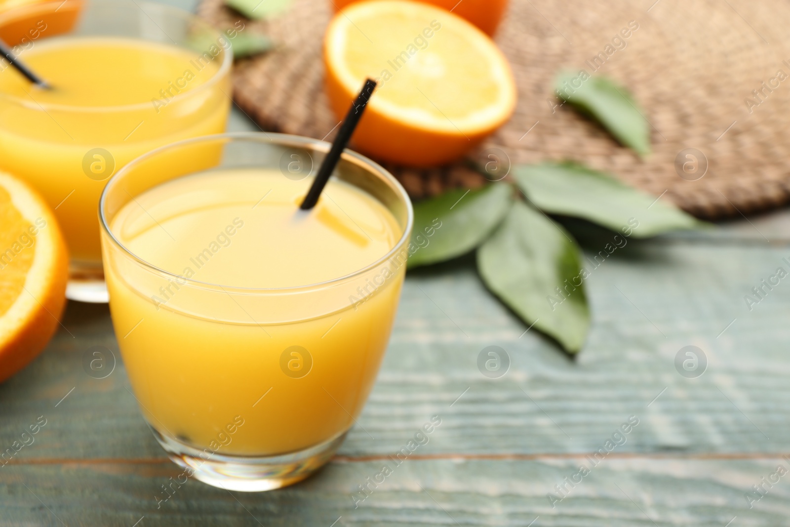 Photo of Delicious orange juice on light blue wooden table, closeup. Space for text