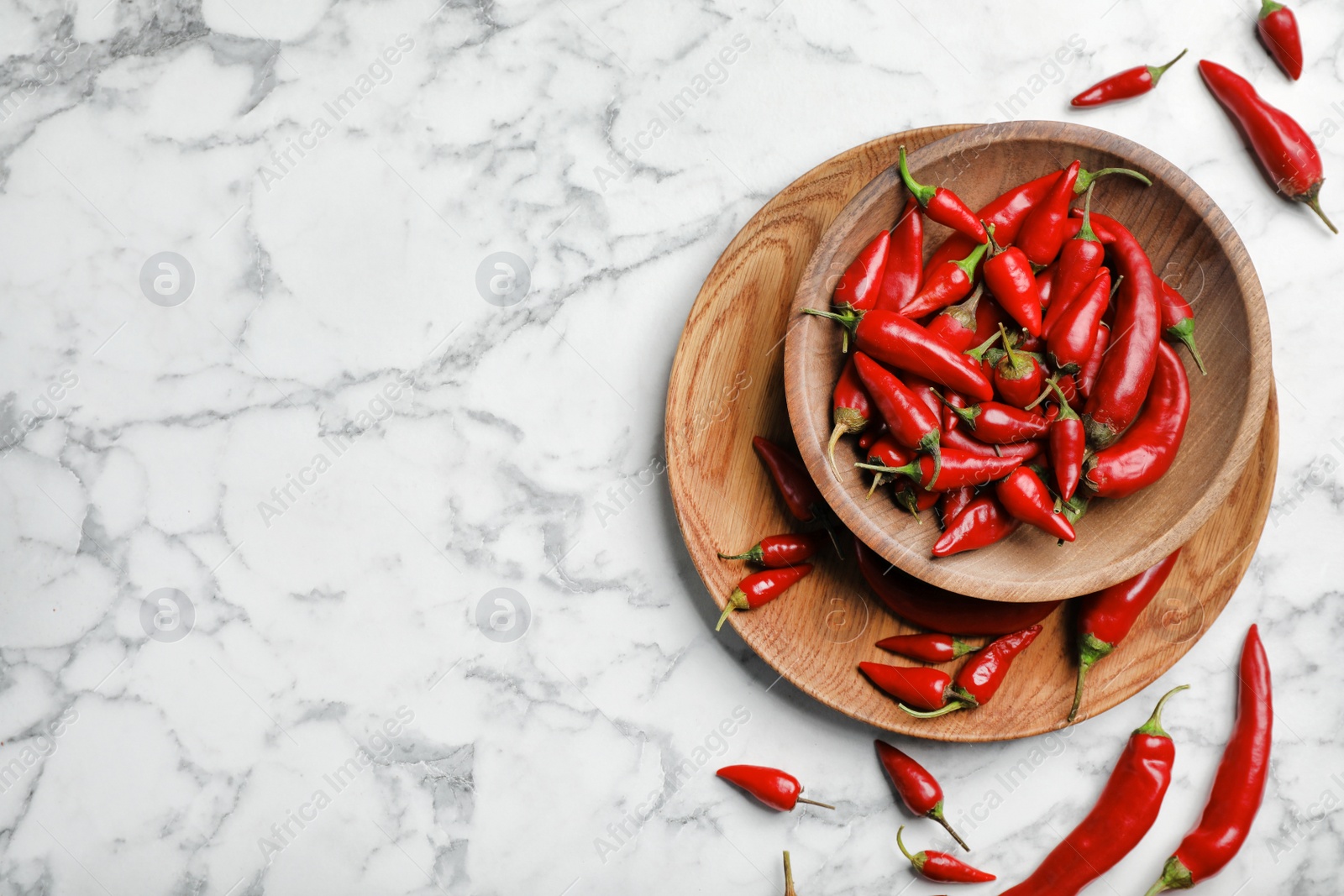 Photo of Wooden dishware and red chili peppers on marble background, top view with space for text