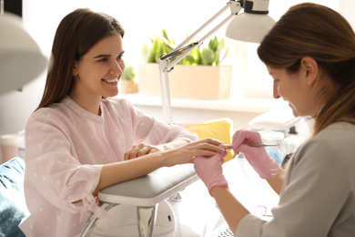 Professional manicurist working with client in beauty salon