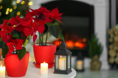 Photo of Potted poinsettias, burning candles and festive decor on white table in room, space for text. Christmas traditional flower