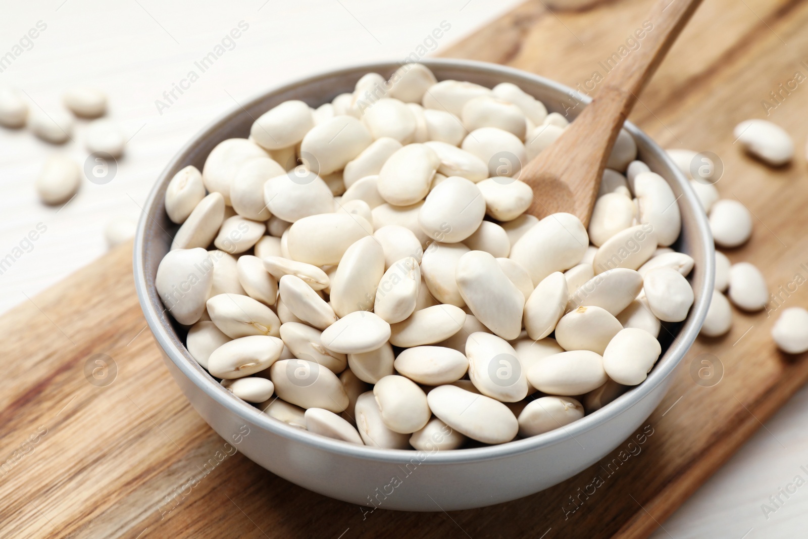Photo of Raw beans and spoon in bowl on wooden board, closeup