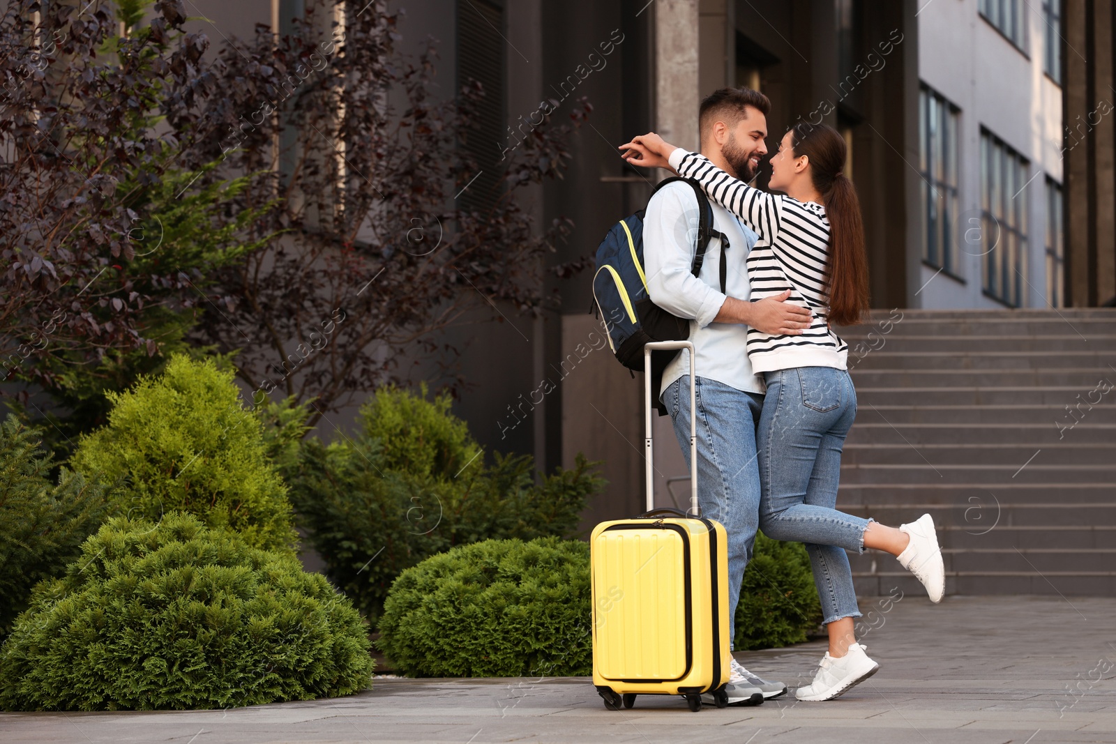 Photo of Long-distance relationship. Beautiful young couple with luggage hugging near building outdoors