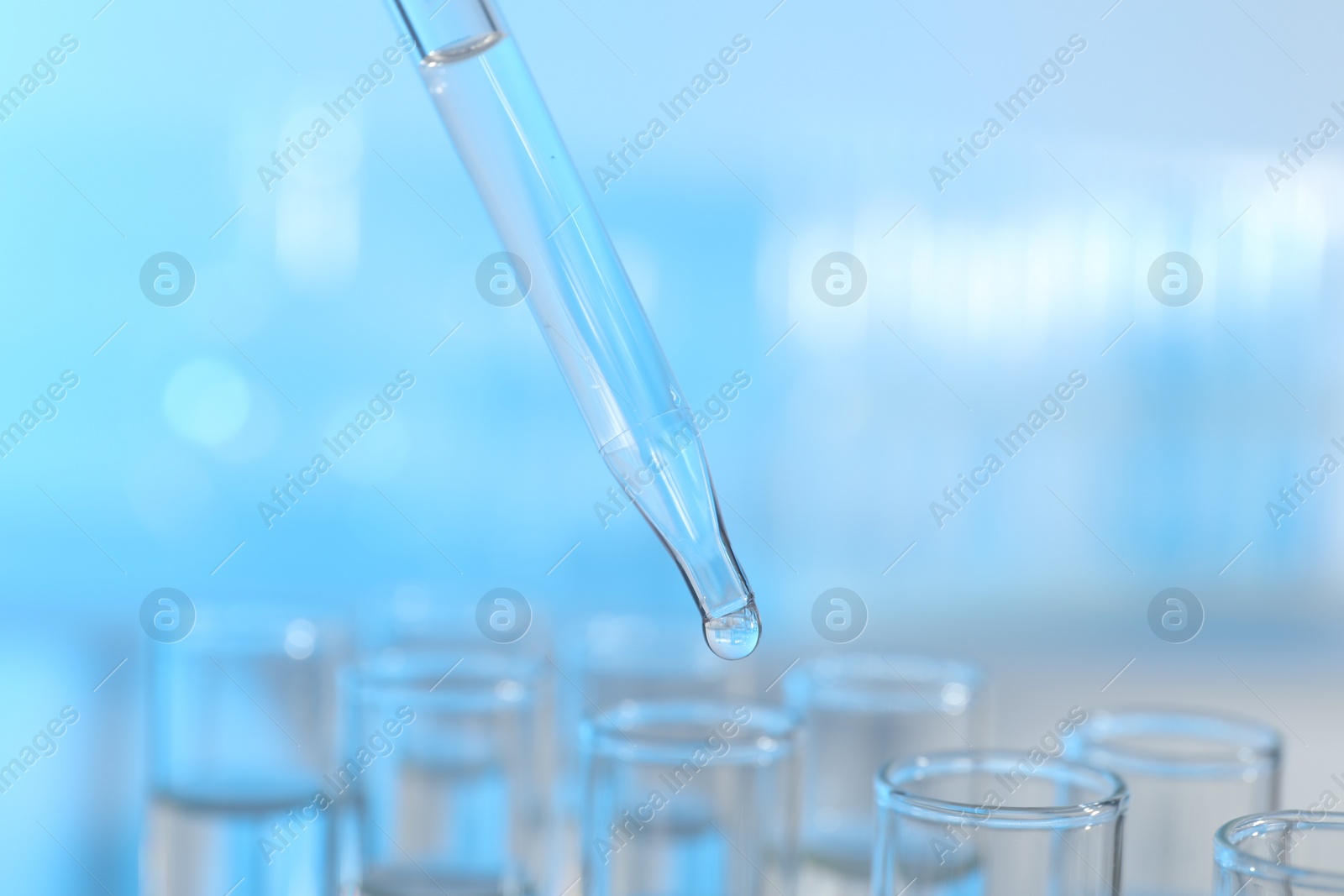 Photo of Dripping liquid from pipette into test tube on light background, closeup