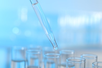 Photo of Dripping liquid from pipette into test tube on light background, closeup