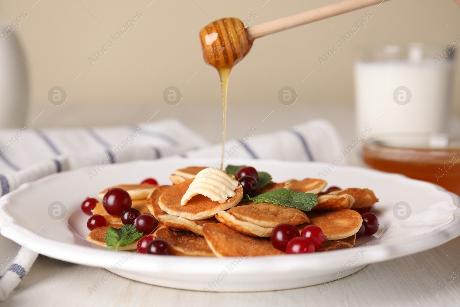 Photo of Pouring honey onto cereal pancakes with cranberries at white wooden table