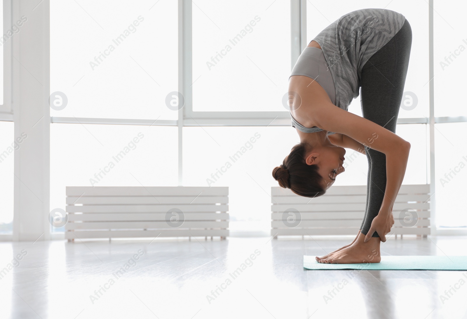 Photo of Young woman practicing standing forward bend asana in yoga studio. Uttanasana pose