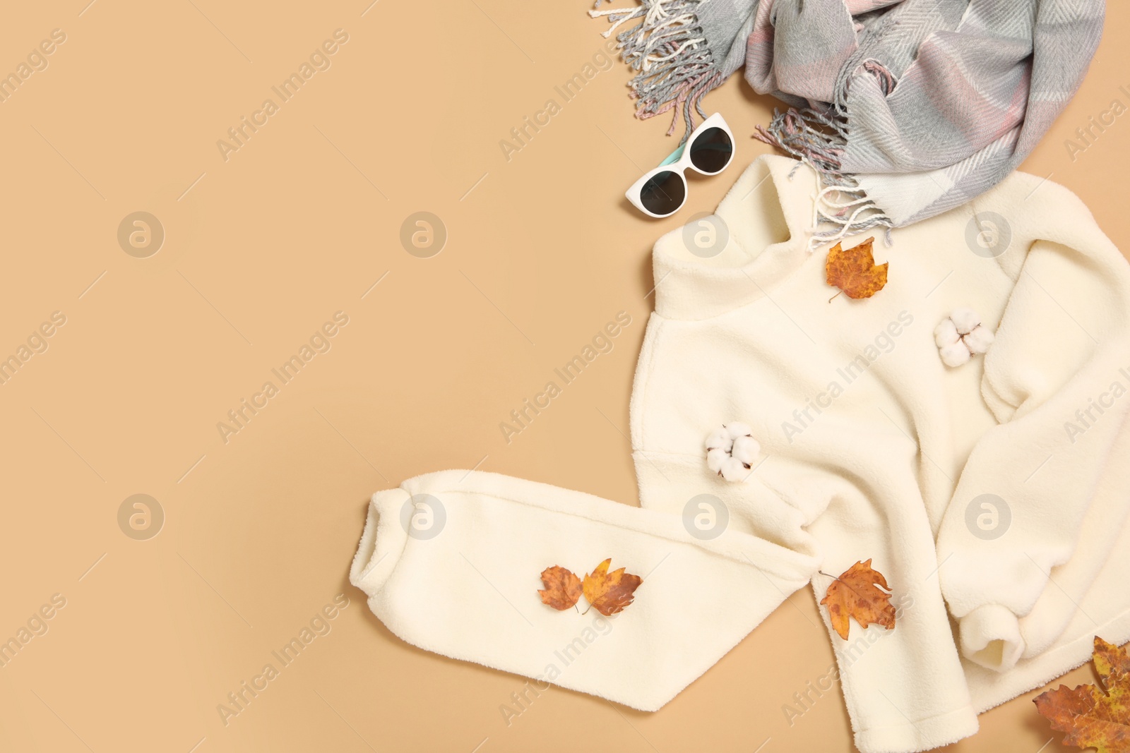 Photo of Sweater, scarf and dry leaves on beige background, flat lay with space for text. Autumn season