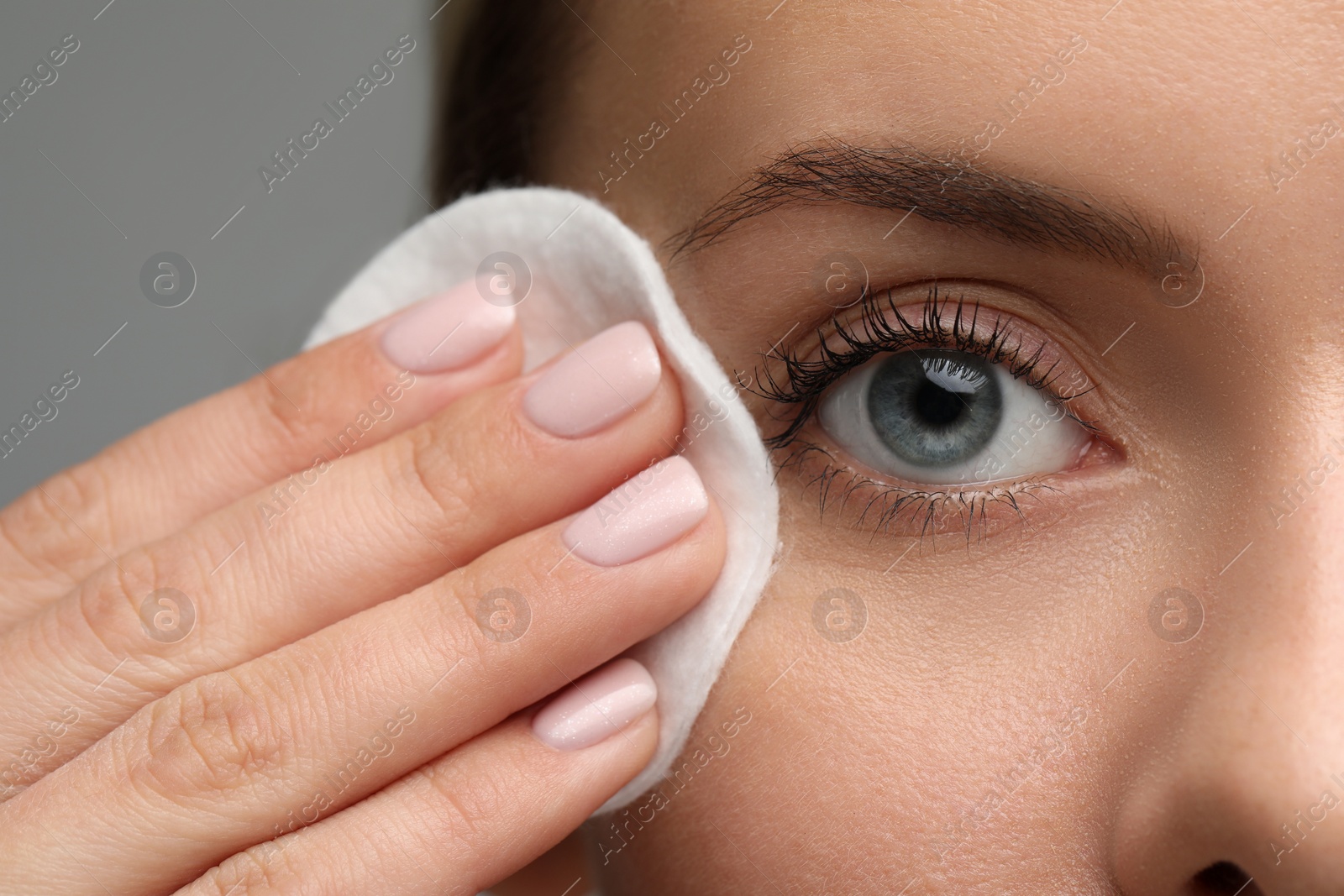 Photo of Beautiful woman removing makeup with cotton pad on grey background, closeup