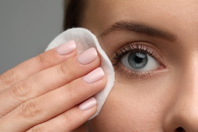 Photo of Beautiful woman removing makeup with cotton pad on grey background, closeup