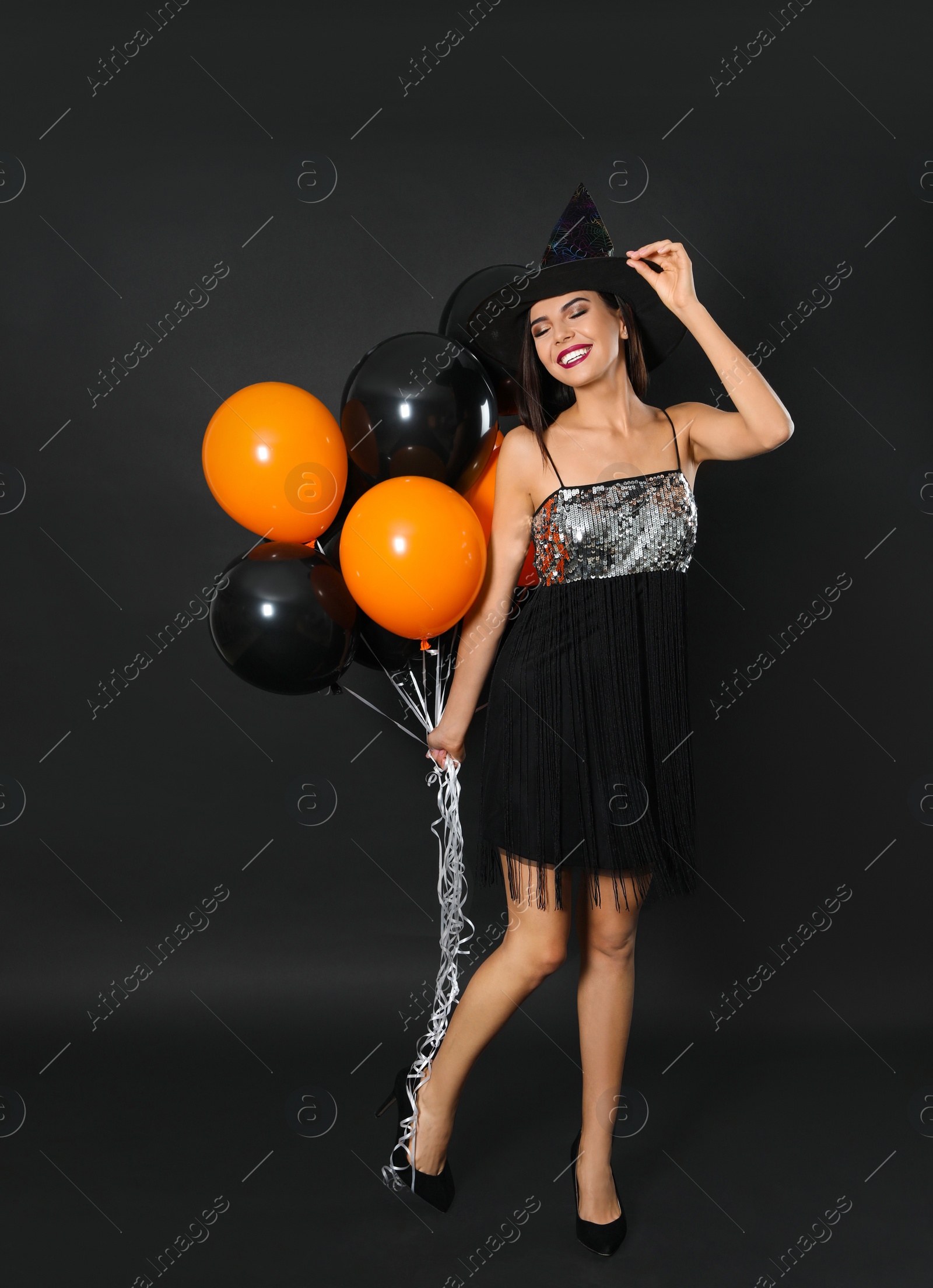 Photo of Beautiful woman wearing witch costume with balloons for Halloween party on black background