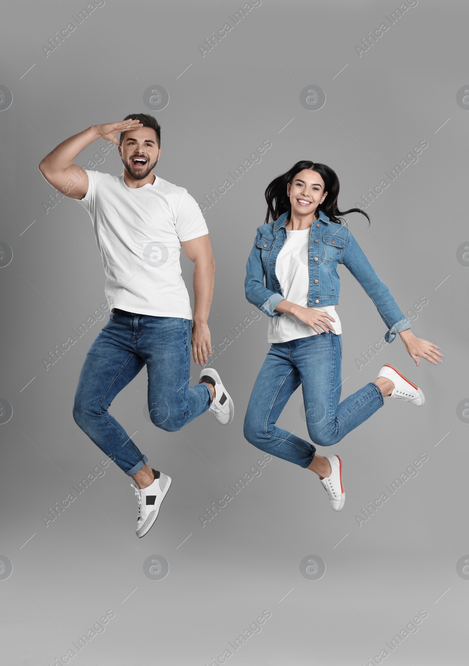 Photo of Young couple in stylish jeans jumping on grey background