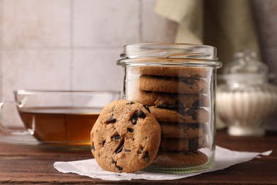 Photo of Glass jar with delicious chocolate chip cookies and tea on wooden table