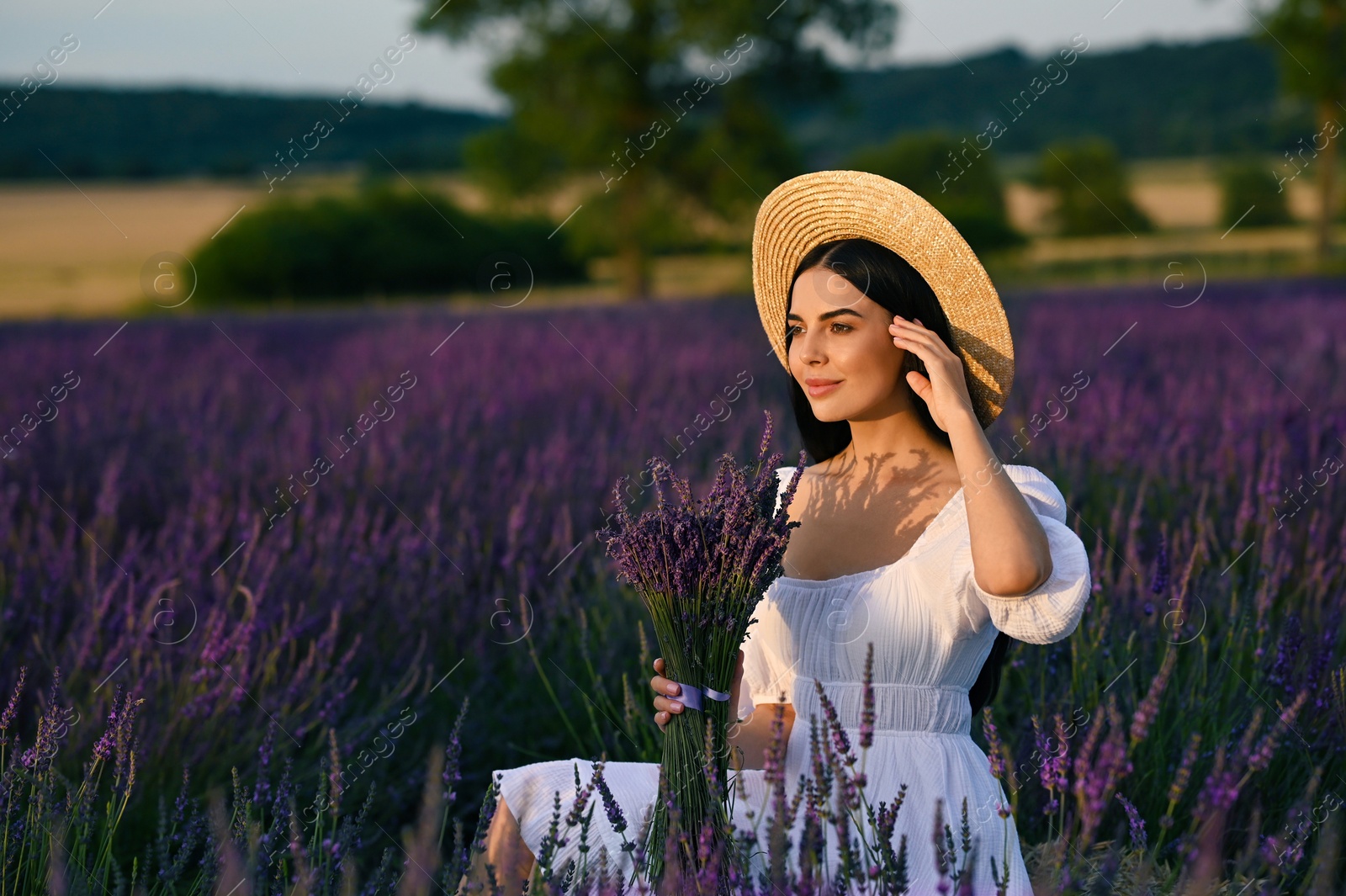 Photo of Beautiful young woman with bouquet sitting in lavender field