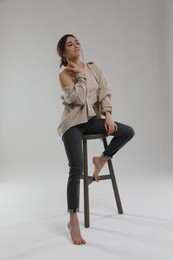 Portrait of beautiful woman sitting on chair against light grey background