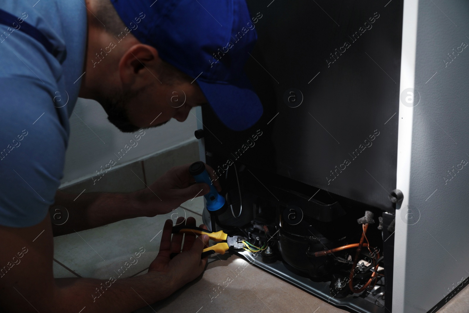 Photo of Professional electrician with flashlight fixing refrigerator indoors