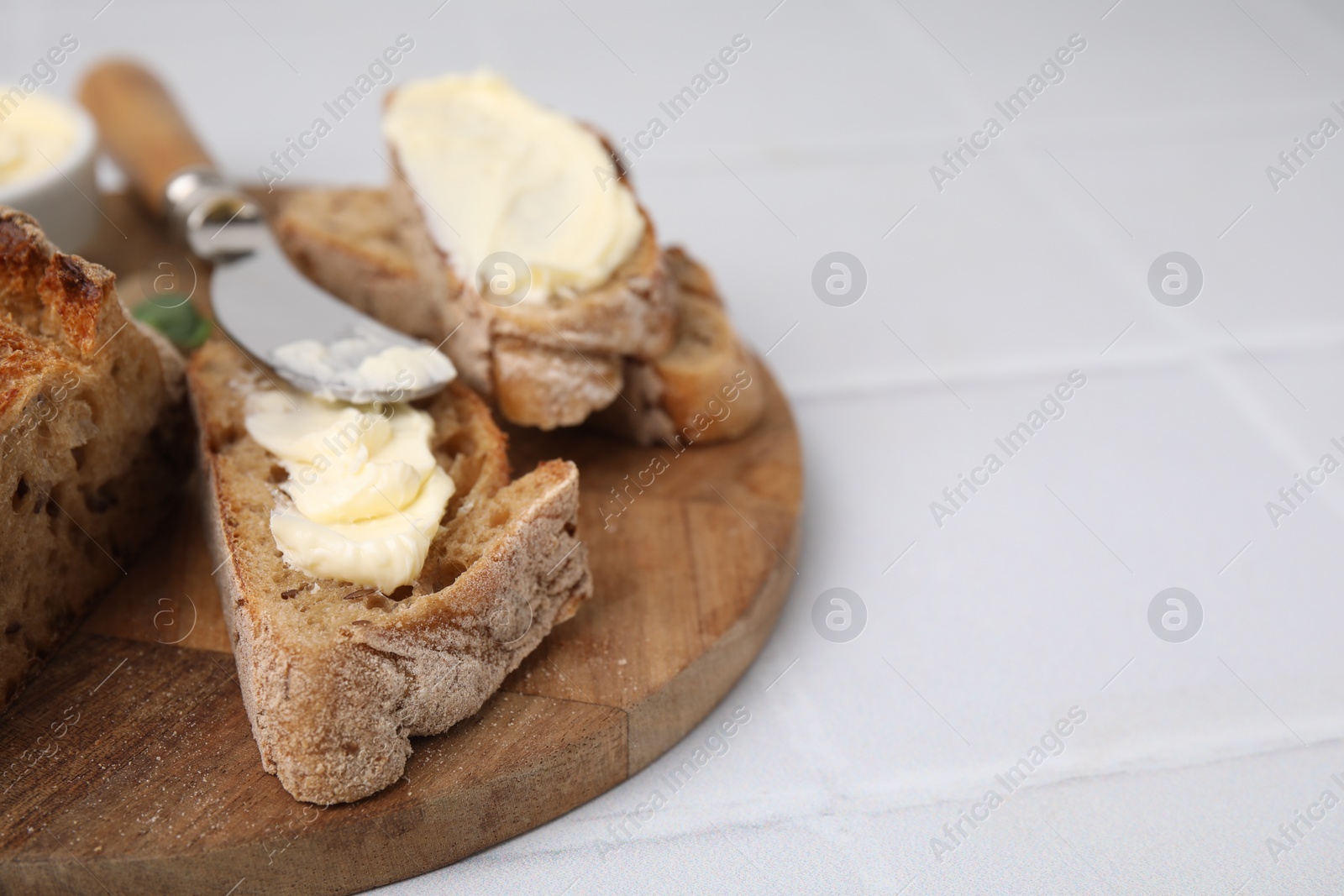 Photo of Tasty bread with butter and knife on white tiled table, closeup. Space for text