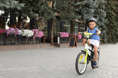 Photo of Happy little boy in helmet riding bicycle on street