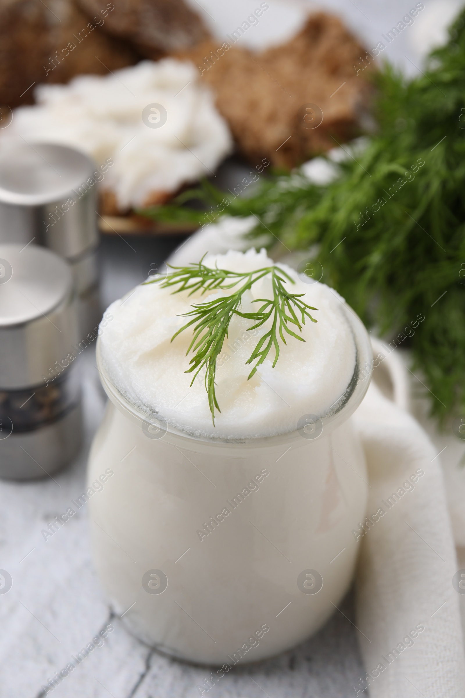 Photo of Delicious pork lard with dill in glass jar on light textured table, closeup