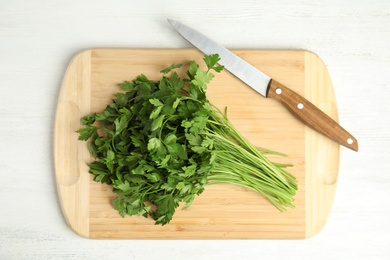 Photo of Board with fresh green parsley and knife on wooden background, top view