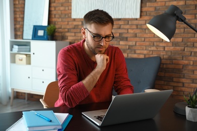 Photo of Young man using laptop at table indoors