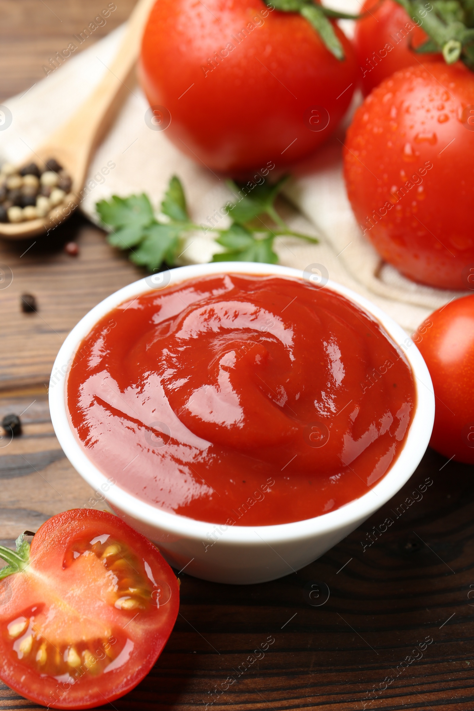 Photo of Delicious ketchup in bowl and tomatoes on wooden table, closeup