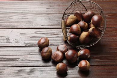 Photo of Sweet fresh edible chestnuts in metal basket on wooden table, space for text