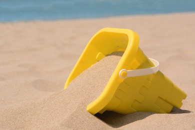 Photo of Yellow plastic bucket on sand near sea, closeup. Beach toy