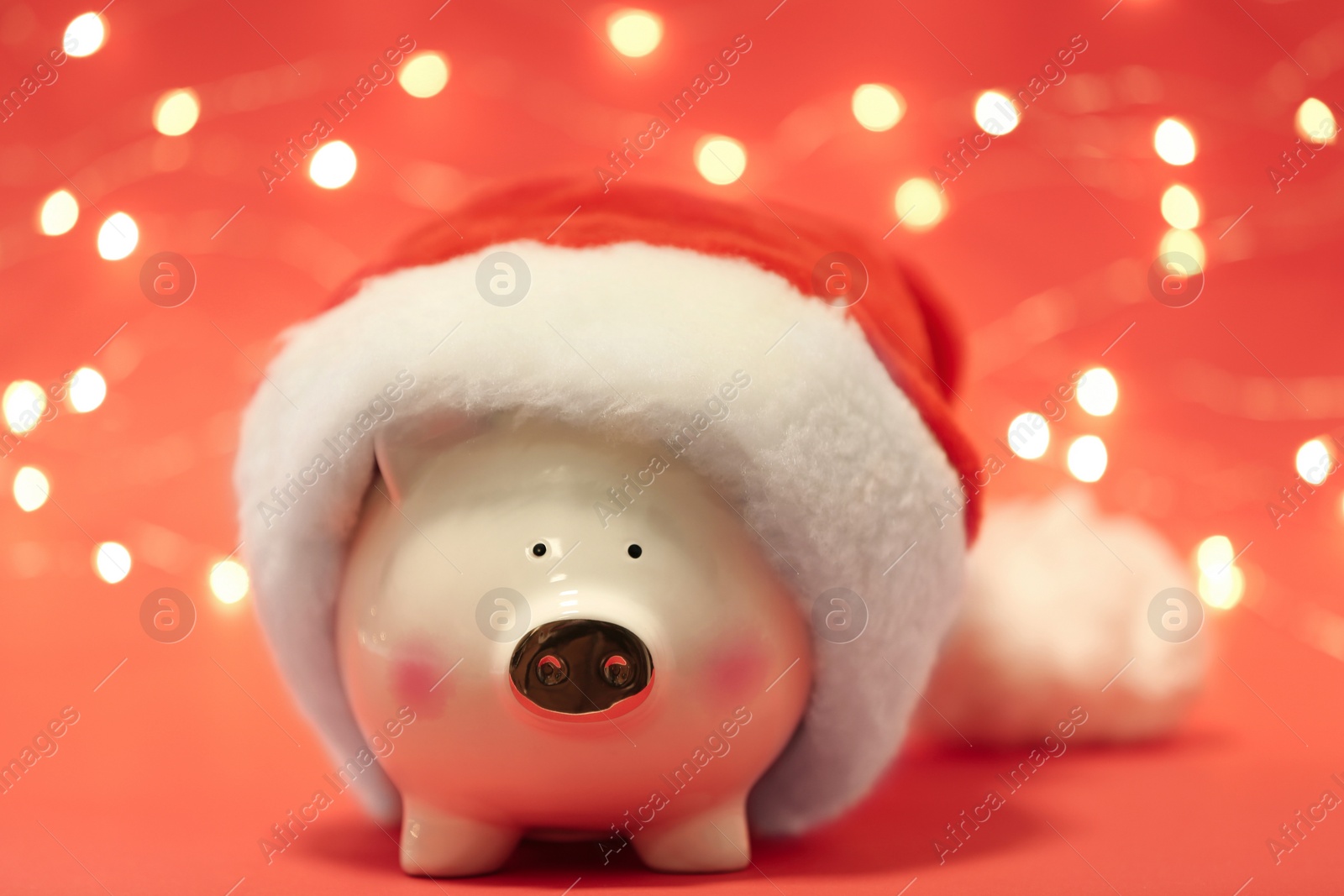 Photo of Cute piggy bank with Santa hat against blurred Christmas lights