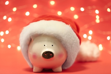 Cute piggy bank with Santa hat against blurred Christmas lights