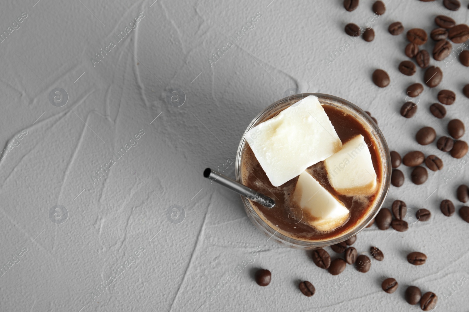 Photo of Coffee drink with milk ice cubes and beans on grey background, top view. Space for text