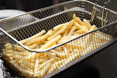 Cooking delicious french fries in hot oil, closeup