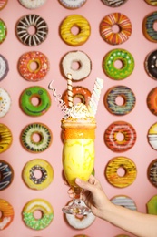 Woman holding glass of tasty milk shake with sweets near decorated wall, closeup