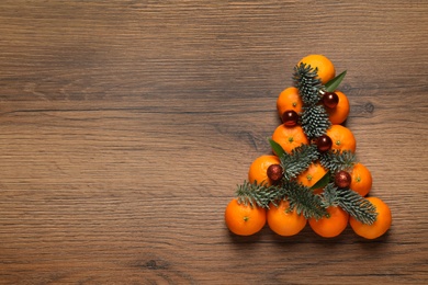 Photo of Christmas tree shape made of tangerines on wooden background, flat lay. Space for text