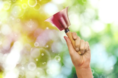 Woman with school bell outdoors, closeup. Bokeh effect