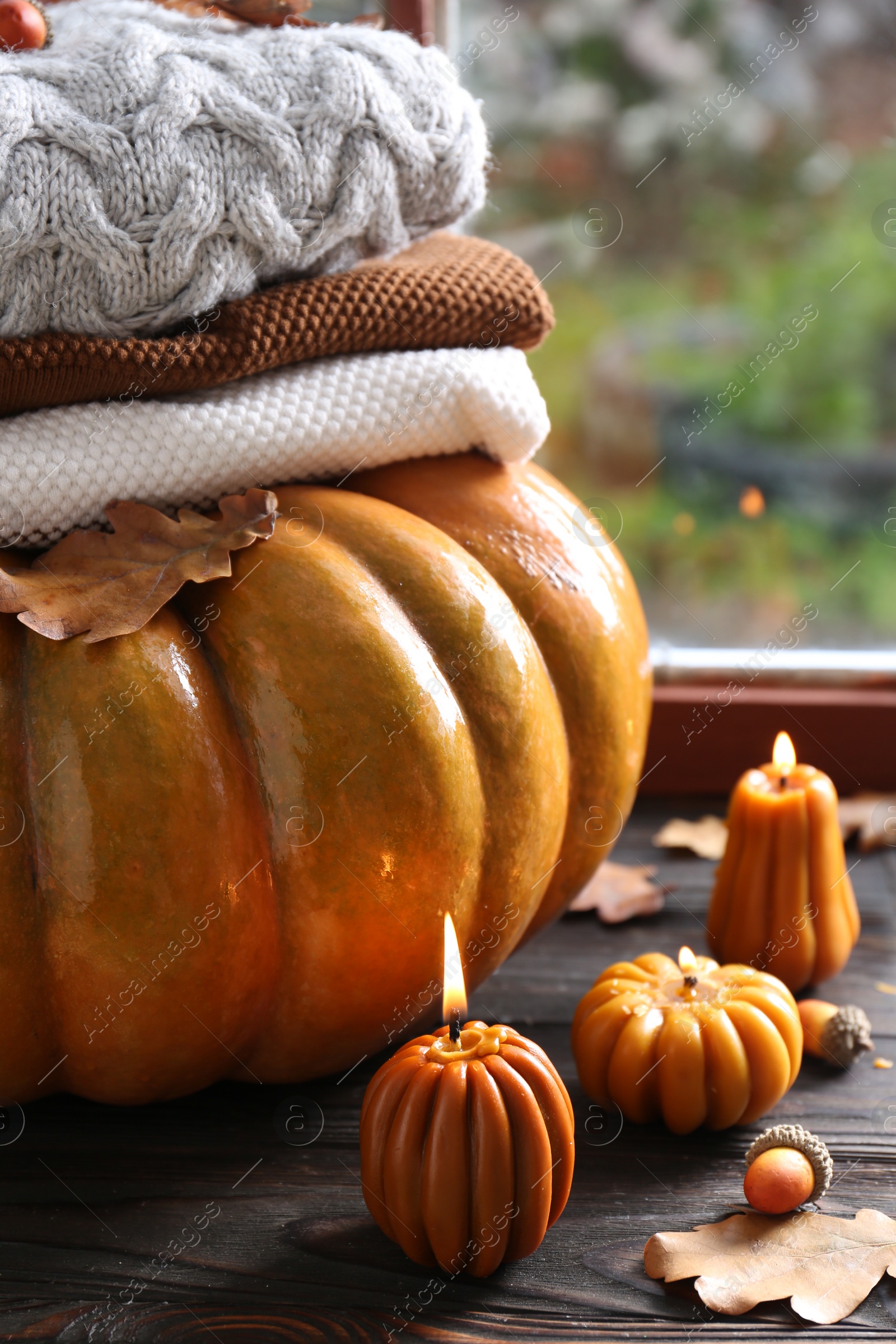 Photo of Beautiful burning candles in shape of pumpkins on wooden table near window. Autumn atmosphere