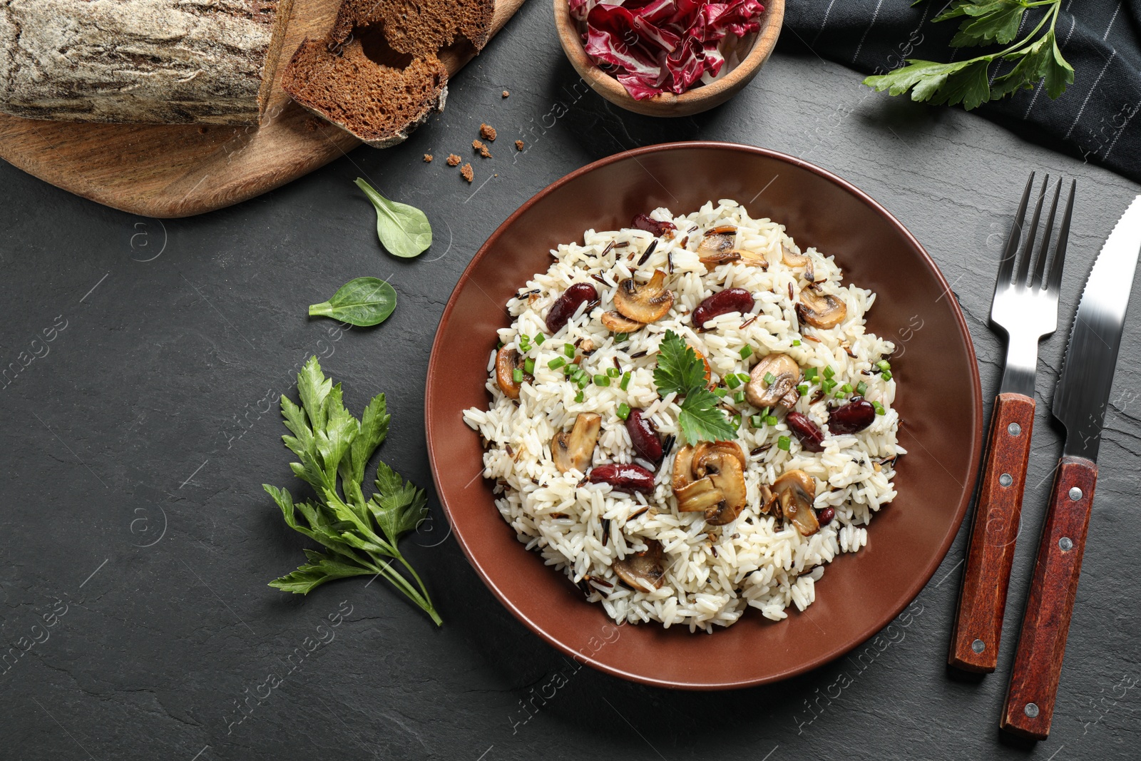 Photo of Delicious rice pilaf with mushrooms served on black table, flat lay