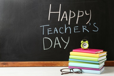 Blackboard with inscription HAPPY TEACHER'S DAY and books on white wooden table