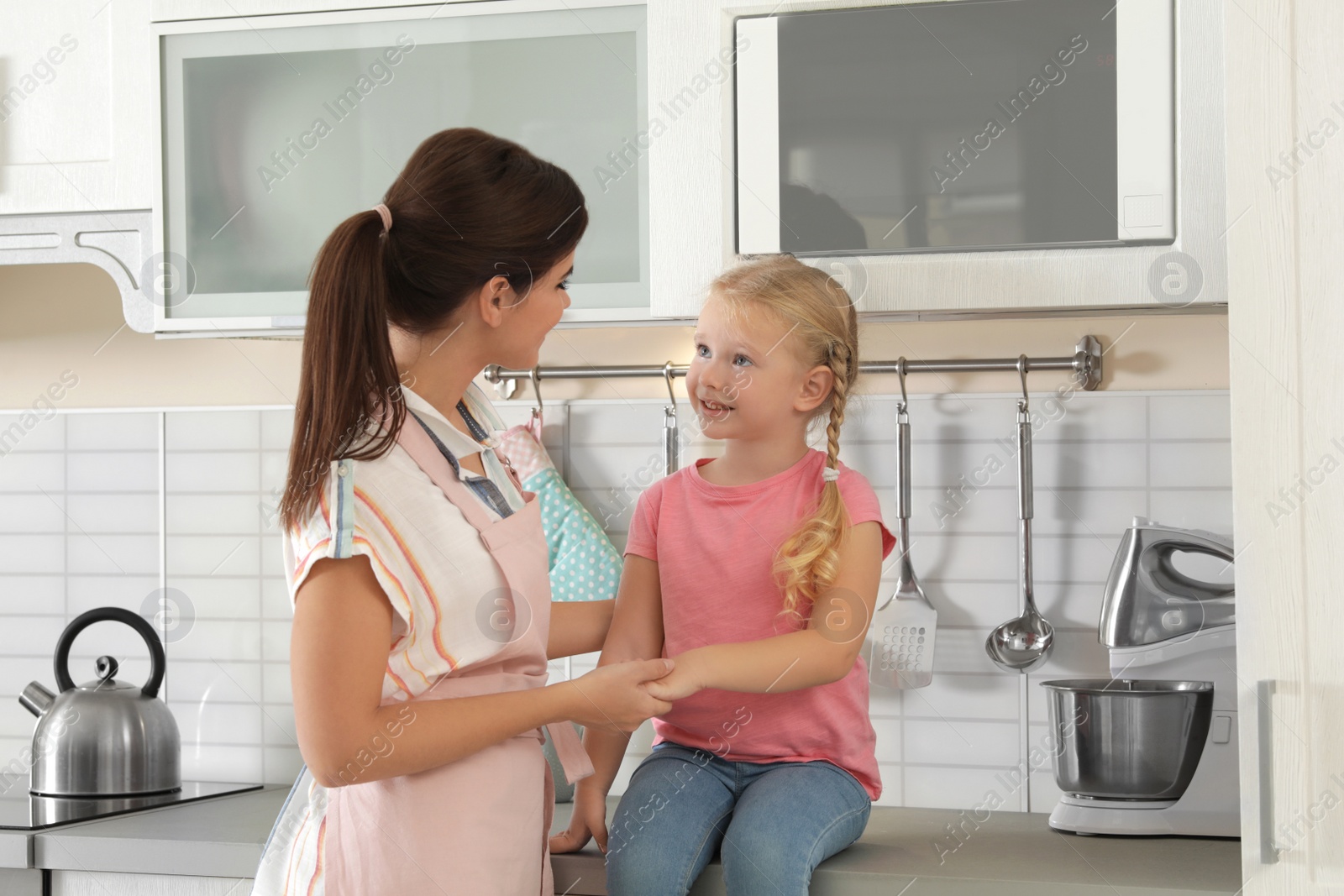 Photo of Young beautiful woman and her daughter near microwave oven in kitchen