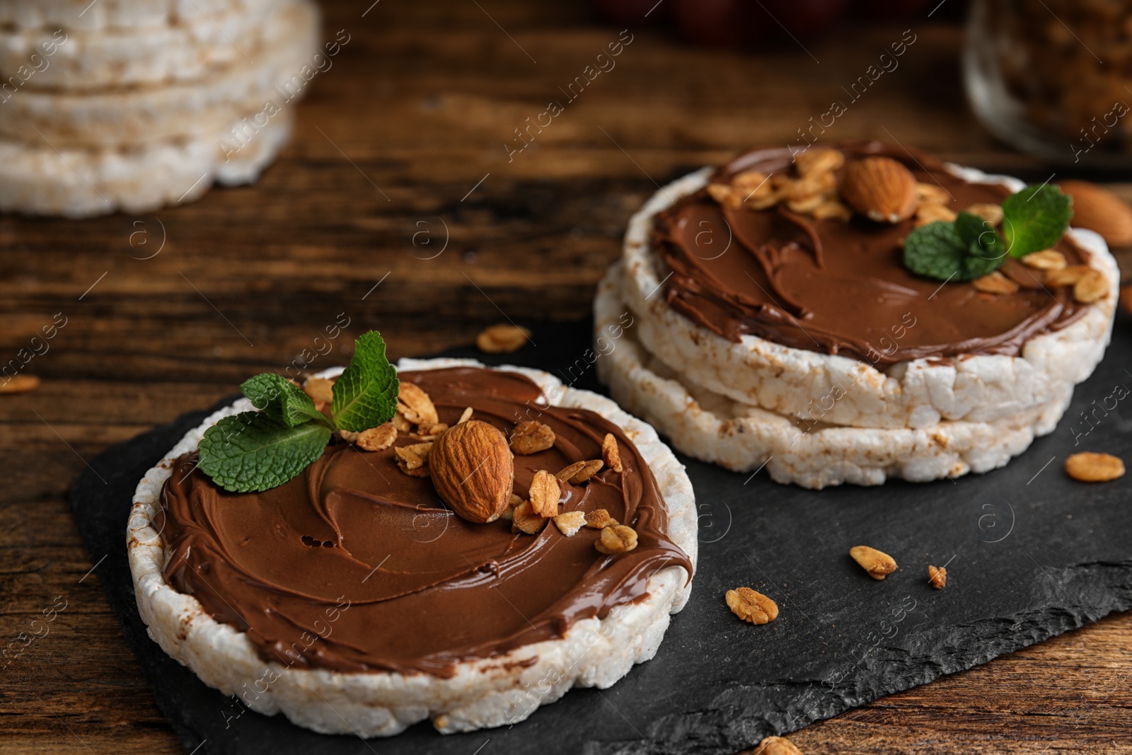 Photo of Puffed rice cakes with chocolate spread, nuts and mint on wooden table, closeup