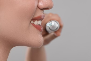 Photo of Woman brushing her teeth with electric toothbrush on light grey background, closeup. Space for text