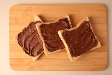 Tasty toasts with chocolate paste on beige background, top view