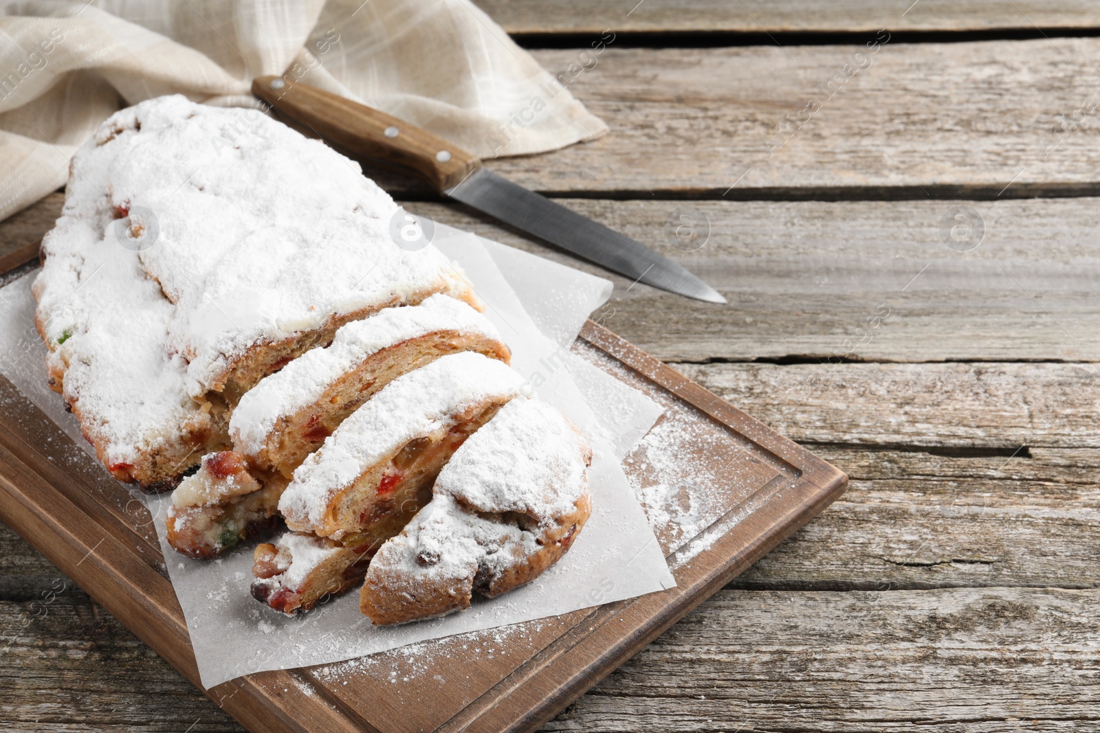 Photo of Traditional Christmas Stollen with icing sugar on wooden table, space for text