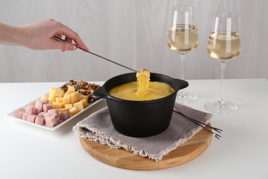 Photo of Dipping piece of ham into fondue pot with tasty melted cheese at white table, closeup