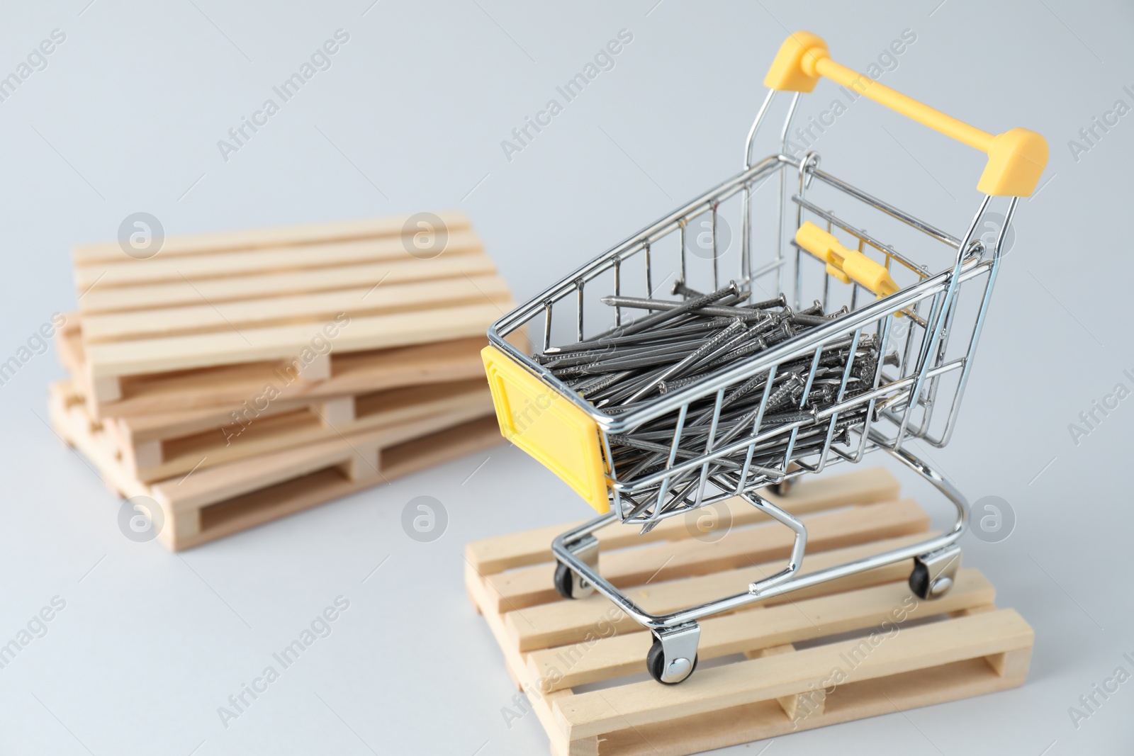 Photo of Metal nails in shopping cart on light grey background, space for text