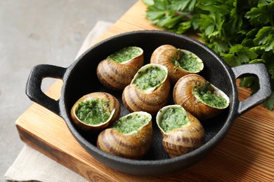 Delicious cooked snails in baking dish on grey table, closeup