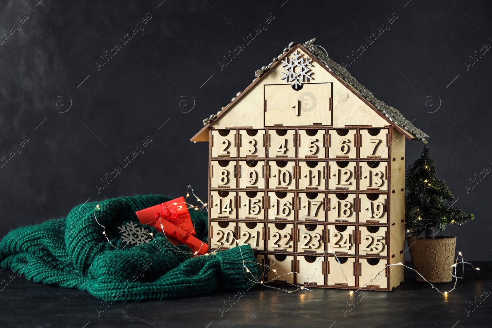 Photo of House shaped Christmas advent calendar, knitted sweater and festive decor on black table