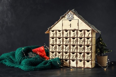 Photo of House shaped Christmas advent calendar, knitted sweater and festive decor on black table
