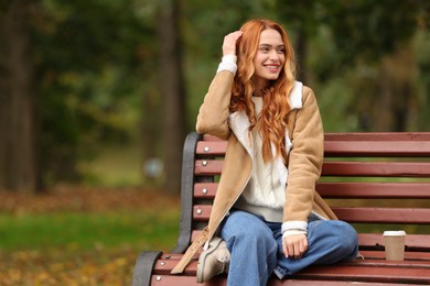Photo of Portrait of smiling woman sitting on bench in autumn park. Space for text