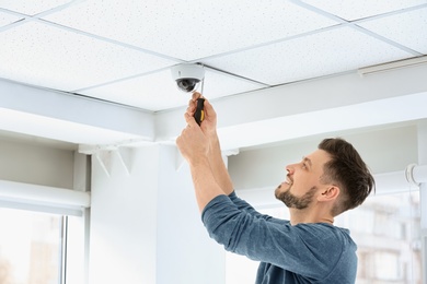 Photo of Technician installing CCTV camera on ceiling indoors