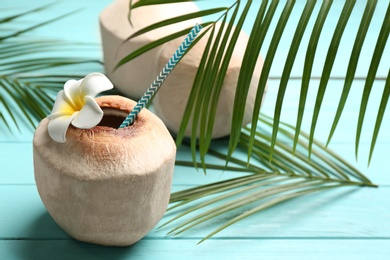 Photo of Young peeled coconuts with palm leaves and flower on light blue wooden table